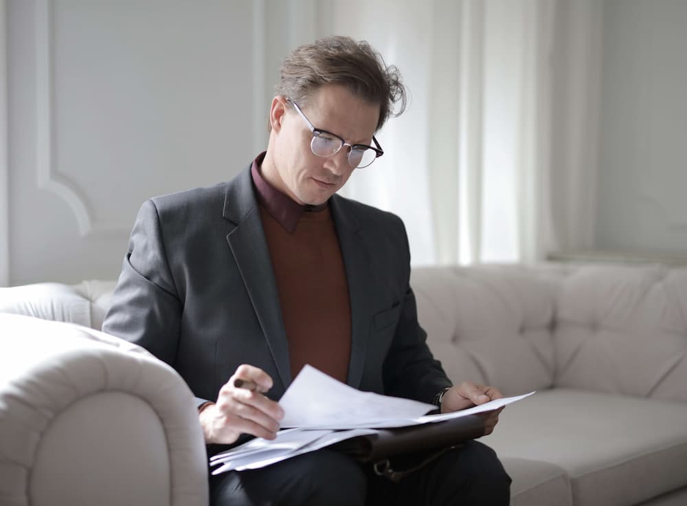 a man in a suit sitting on a couch reading a paper