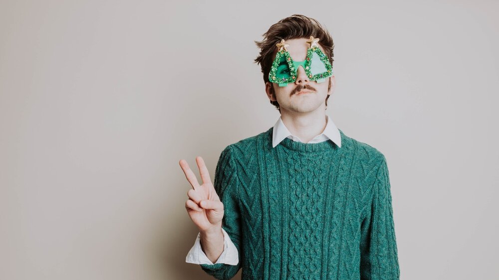 a man in a green sweater and white shirt holding up his peace sign