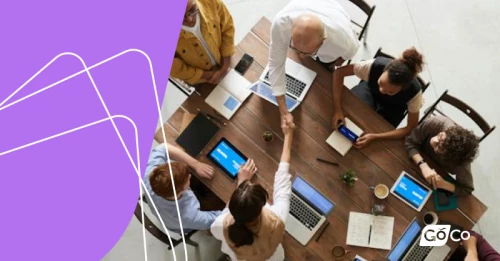 a group of people sitting around a table with laptops