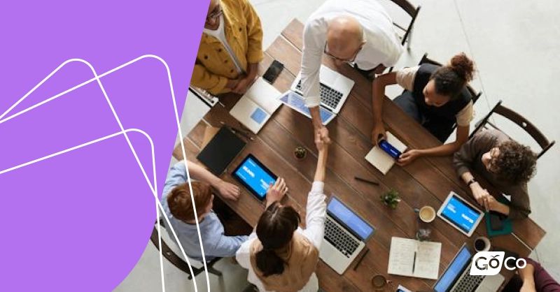 a group of people sitting around a table with laptops
