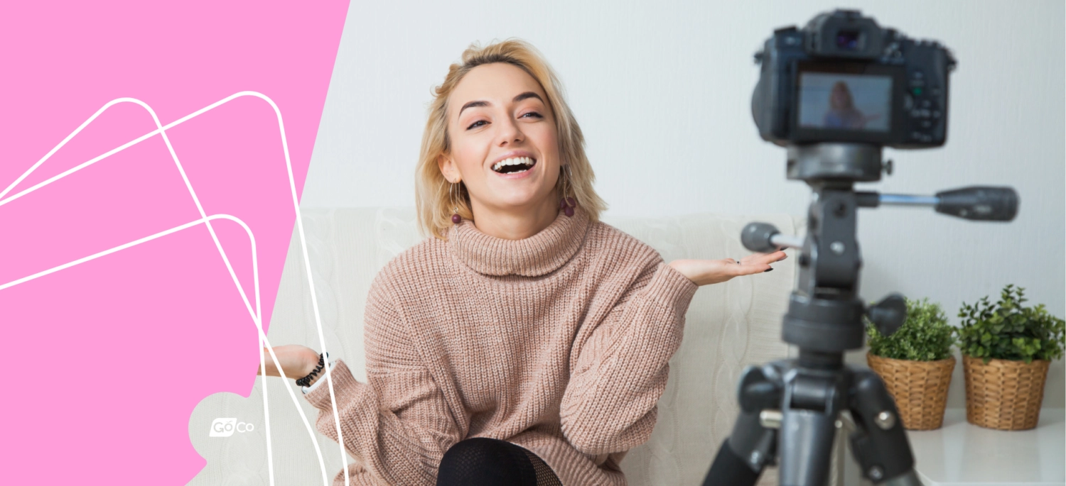 a woman sitting on a couch with a camera and a pink background