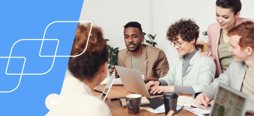 a group of people sitting around a table with laptops