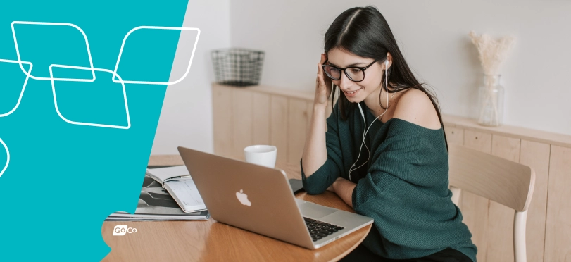 An HR manager wearing earbuds taking a break to listen to a podcast on her laptop