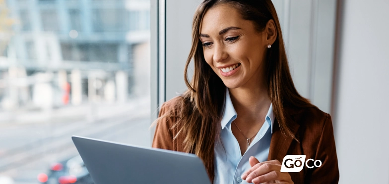 a woman looking at her laptop while sitting in front of a window