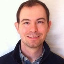 a man in a blue jacket standing against a white wall